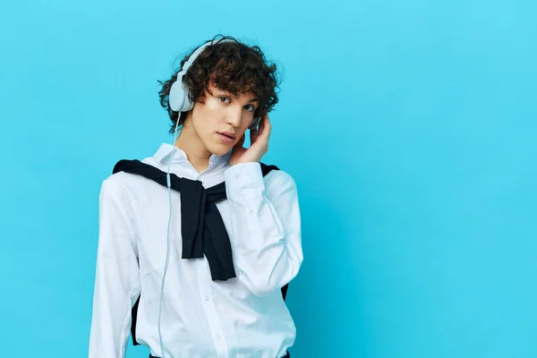 Cara encaracolado tecnologia fones de ouvido em uma camisa branca com suéter fundo azul — Fotografia de Stock