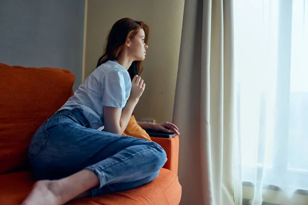 Женщина сидит на оранжевом диване дома в защитных масках стиль жизни — стоковое фото