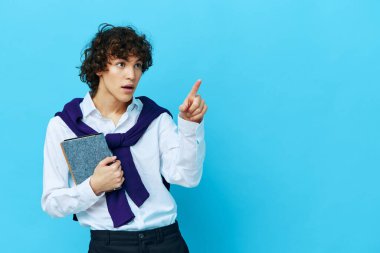 Omuzlarında süveter tişörtü olan mavi arka planda not defteri olan öğrenci.