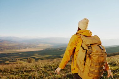 Sırt çantalı sarı ceketli bir kadın gezgin dağlarda dinleniyor.