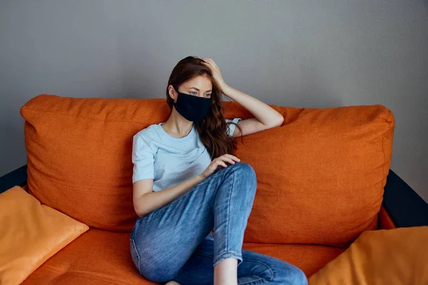 Triste donna in nero maschere protettive seduto sul divano a casa quarantena — Foto Stock