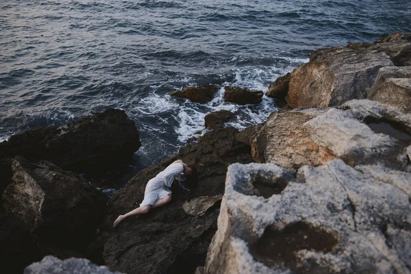 白いドレス姿の野生の岩肌の海岸にひっそりと佇む官能的な女性 — ストック写真