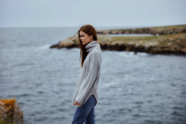 Belle femme dans un pull gris se tient sur un rivage rocheux nature Lifestyle — Photo