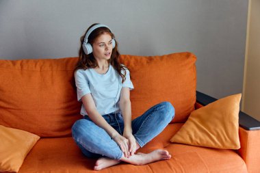 Turuncu koltukta oturmuş kulaklıkla müzik dinleyen bir kadının portresi. Yüksek kalite fotoğraf