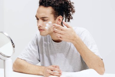 Yakışıklı adam yüzüne krem sürüyor ve aynaya bakıyor. Kozmetik kesimi manzarası var. Yüksek kalite fotoğraf