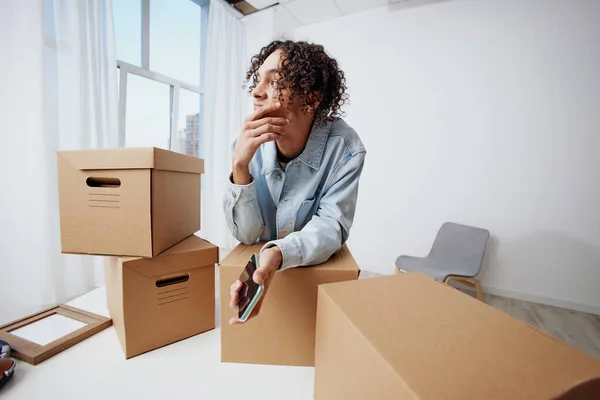 Un hombre joven cajas de cartón en la habitación desempacar con el interior del teléfono — Foto de Stock