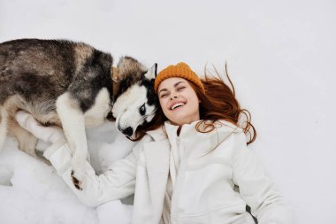 Karda genç bir kadın köpekle oynuyor. Eğlenceli bir arkadaşlık havası.