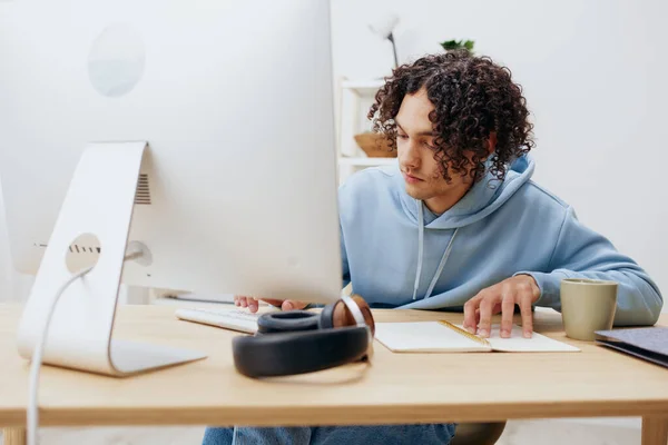 Cara com cabelo encaracolado sentado na frente do computador internet interior online — Fotografia de Stock
