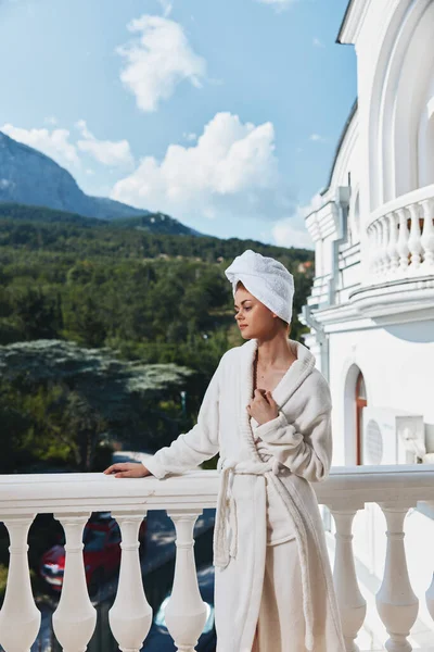 Портрет великолепной женщины с полотенцем на голове в белом халате, остановившейся на балконе отеля — стоковое фото