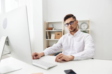 Beyaz tişörtlü yakışıklı iş adamı telefon ofisi olan bir bilgisayarın başında oturuyor.