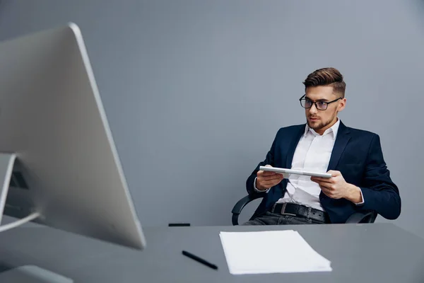 Manager sitzt am Schreibtisch vor einem Computer grauer Hintergrund — Stockfoto