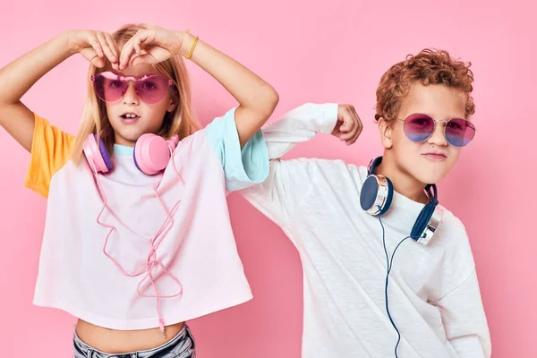 Divertido niño y niña auriculares de entretenimiento jugando fondo de color rosa — Foto de Stock