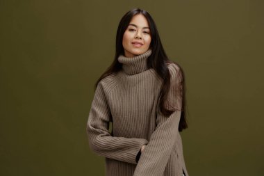 Süveter giyen, gülümseyen, yeşil arka planlı bir kadın portresi.