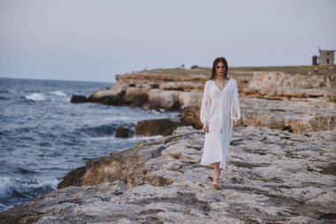 Güzel kadın beyaz elbisesi açık havada özgürce duruyor.