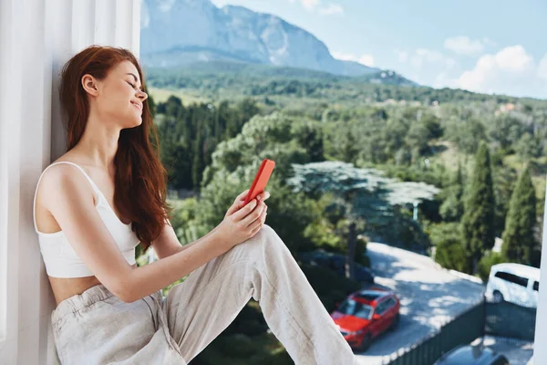 Jovem mulher atraente sentado na varanda com telefone bela vista montanha verão inalterado — Fotografia de Stock