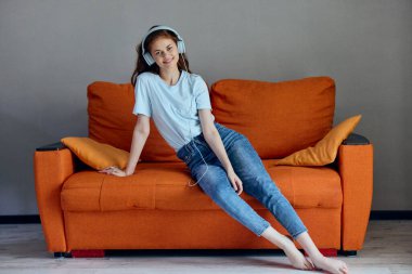 Güzel bir kadın evdeki kanepede oturmuş kulaklıkla müzik dinliyor.