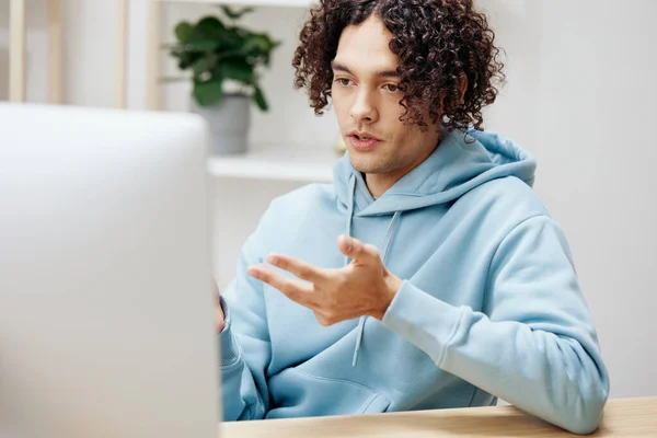 Хлопець з кучерявим волоссям, сидячи за столом перед комп'ютером позаштатний інтер'єр — стокове фото