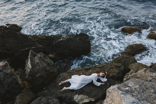 Attractive woman with long hair in a secluded spot on a wild rocky coast in a white dress unaltered — Stock Photo, Image