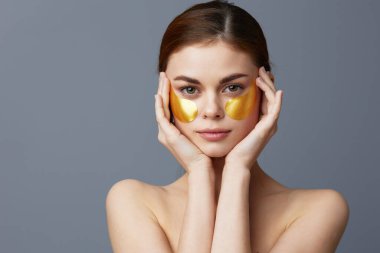 Genç kadın altın yamalar, temiz ten tebessümü, gri arka plan.