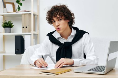 Dizüstü bilgisayarın önünde beyaz koltukta oturan kıvırcık adam yaşam tarzı teknolojisini öğreniyor.