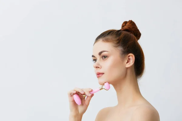 Pretty woman jade face massager wrinkle smoothing tied hair in a bun isolated background — Stock Photo, Image