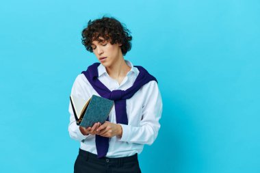 Omuzlarında kazak olan not defterli bir adam mavi arka planda.