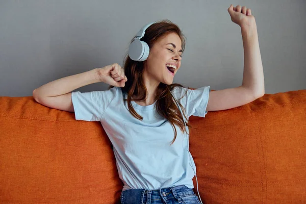 Bela mulher sentada no sofá em casa ouvindo música em tecnologias de fones de ouvido — Fotografia de Stock