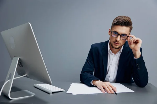 Un homme en costume assis à un bureau devant un ordinateur fond gris — Photo