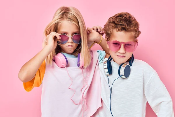 Módní chlapec a dívka nosí sluchátka pózování růžové barvy pozadí — Stock fotografie