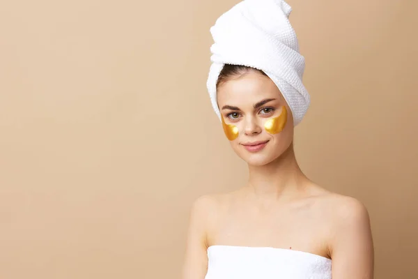 Mooie vrouw gouden vlekken op het gezicht met een handdoek op het hoofd beige achtergrond — Stockfoto