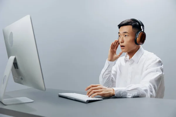 Asijské muž ve sluchátkách u stolu před počítačem izolované pozadí — Stock fotografie
