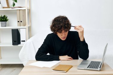 Siyah süveter giyen kıvırcık saçlı adam masada oturuyor.