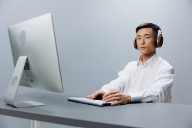 Beyaz gömlekli, kulaklıklı bir işçi ofiste oturuyor.