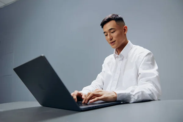 Uomo che lavora su un computer portatile seduto a un tavolo in ufficio sfondo grigio — Foto Stock