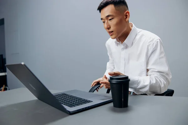 Homem asiático em camisas brancas copo de café senta-se na frente de um escritório de laptop Estilo de vida — Fotografia de Stock