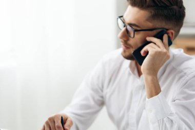 Beyaz gömlekli bir yönetici telefon teknolojisi olan bir bilgisayarın başında oturuyor.