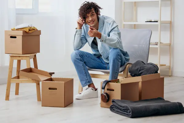 A young man sitting on a chair unpacking with box in hand moving interior