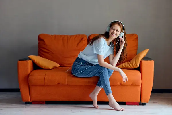 Kadın turuncu koltukta kulaklıkla müzik dinliyor. — Stok fotoğraf