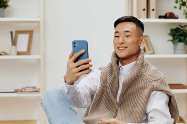 Adam kucağında telefon teknolojisiyle bir odada bir sandalyede oturuyor. Yüksek kalite fotoğraf