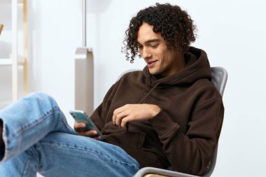 Arka planda telefon olan bir sandalyede oturan genç bir adam. Yüksek kalite fotoğraf