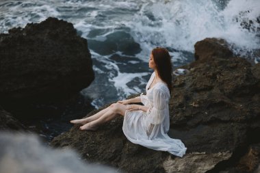 Basik gelinlikli ıslak saçlı kadın taşların üzerinde oturuyor. Yüksek kalite fotoğraf