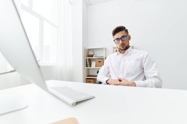 Beyaz gömlekli bir yönetici telefon teknolojisi olan bir bilgisayarın başında oturuyor. Yüksek kalite fotoğraf