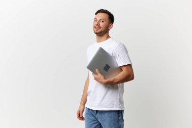 Gülümseyen, bronz tenli yakışıklı, tişörtlü, dizüstü bilgisayarlı beyaz stüdyo arka planında yalnız poz veren yakışıklı bir adam. Uzayın afiş modelini kopyala. Elektronik tamir konsepti