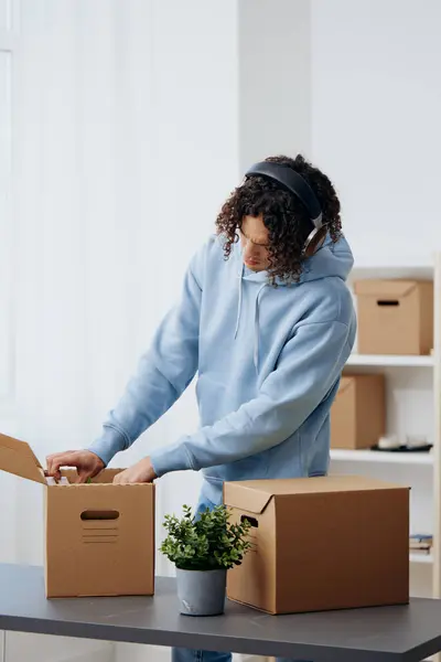 guy with curly hair cardboard boxes in the room unpacking in headphones Lifestyle. High quality photo