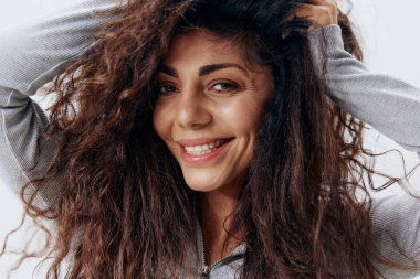 Beyaz Stüdyo Duvarı 'nda izole edilmiş, Gri Süveterli Güzel Latin Kadın Gülümseyen Dokunaklı Kuru Saç Pozu' nun yakın portresi. Moda Mevsimsel Satış Yeni Koleksiyon Kavramı.