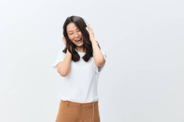 Beyaz tişörtlü mutlu Asyalı kadın kulaklık takıyor gözlerini kapatıyor beyaz stüdyo arka planında izole bir şekilde poz veriyor. Reklam için en iyi teklif. Favori Müzik Uygulaması Reklamı konsepti