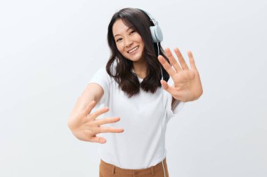 Beyaz tişörtlü mutlu gülümseyen genç Asyalı kadın beyaz stüdyo arka planında izole edilmiş bir şekilde kameraya avuç içi hareketi yapıyor. Reklam için en iyi teklif. Favori Müzik Uygulaması Reklamı konsepti