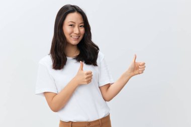 Beyaz tişörtlü neşeli, mutlu Asyalı genç bir kadın beyaz arka planda izole edilmiş iki el hareketi gibi başparmağını kaldırıyor. Reklam için en iyi teklif. İnsanlar yaşam tarzı konsepti. Boş yer