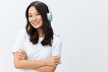 Sevimli, mutlu, beyaz tişörtlü Asyalı genç bir bayan beyaz stüdyo arka planında yalnız poz veriyor. Reklam için en iyi teklif. Favori Müzik Uygulaması Reklamı konsepti
