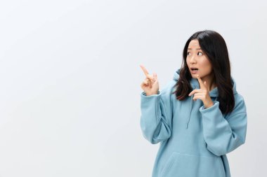 Hey buraya bak. Mavi kapüşonlu kapüşonlu neşeli Asyalı genç kadın beyaz stüdyo arka planında izole edilmiş pozlar vererek fotokopi alanını işaret ediyor. Reklam için en iyi teklif. Moda Yeni Koleksiyon Reklam Konsepti